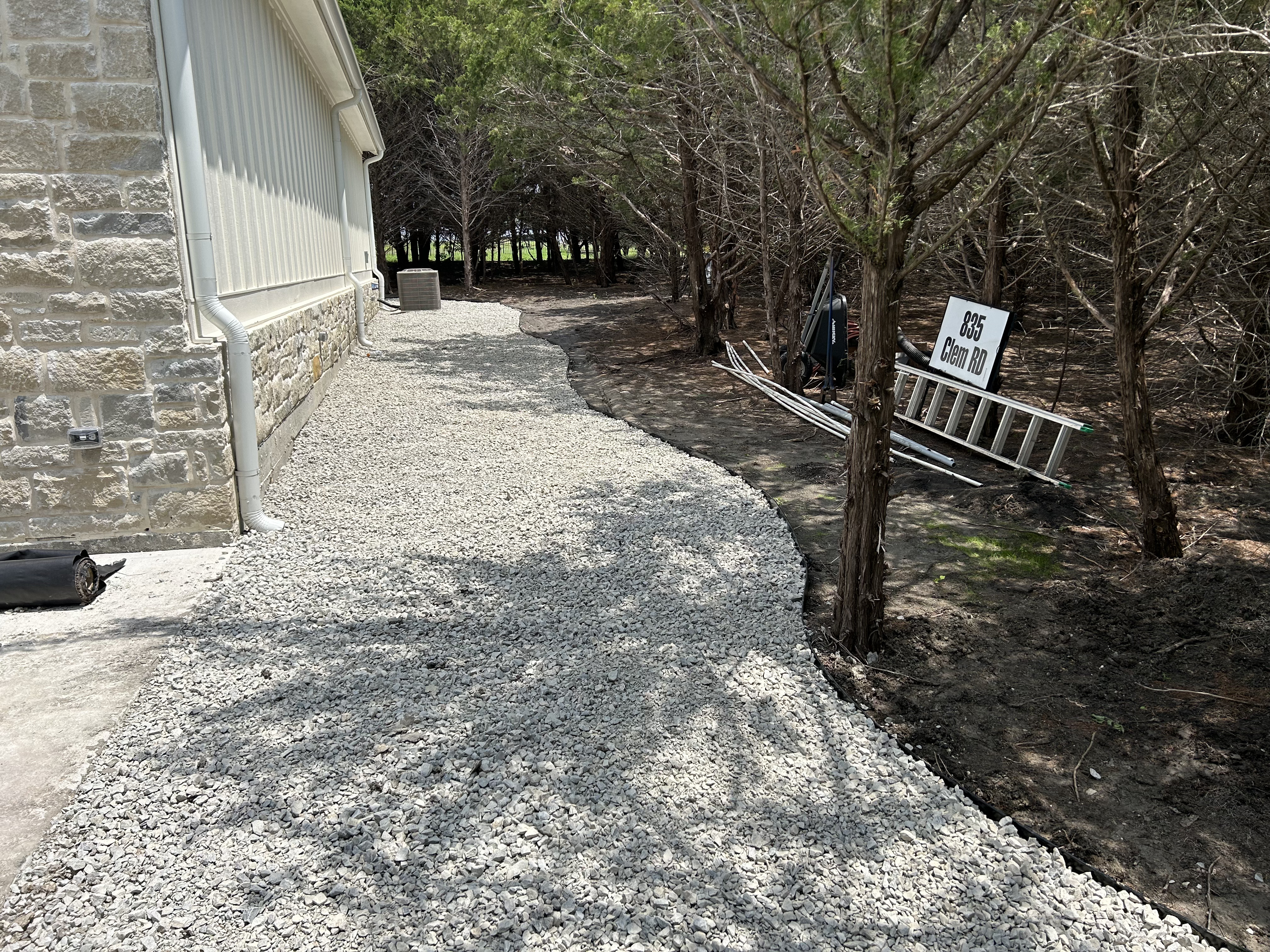 Gravel pathway along side of home with tree-lined edge